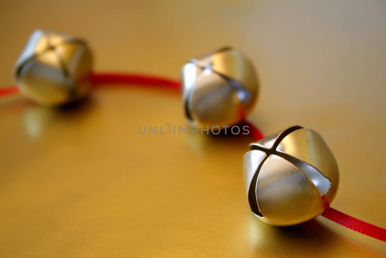 Gold Christmas bells with a red ribbon on a gold metallic background. Used a selective focus and shallow depth of field.