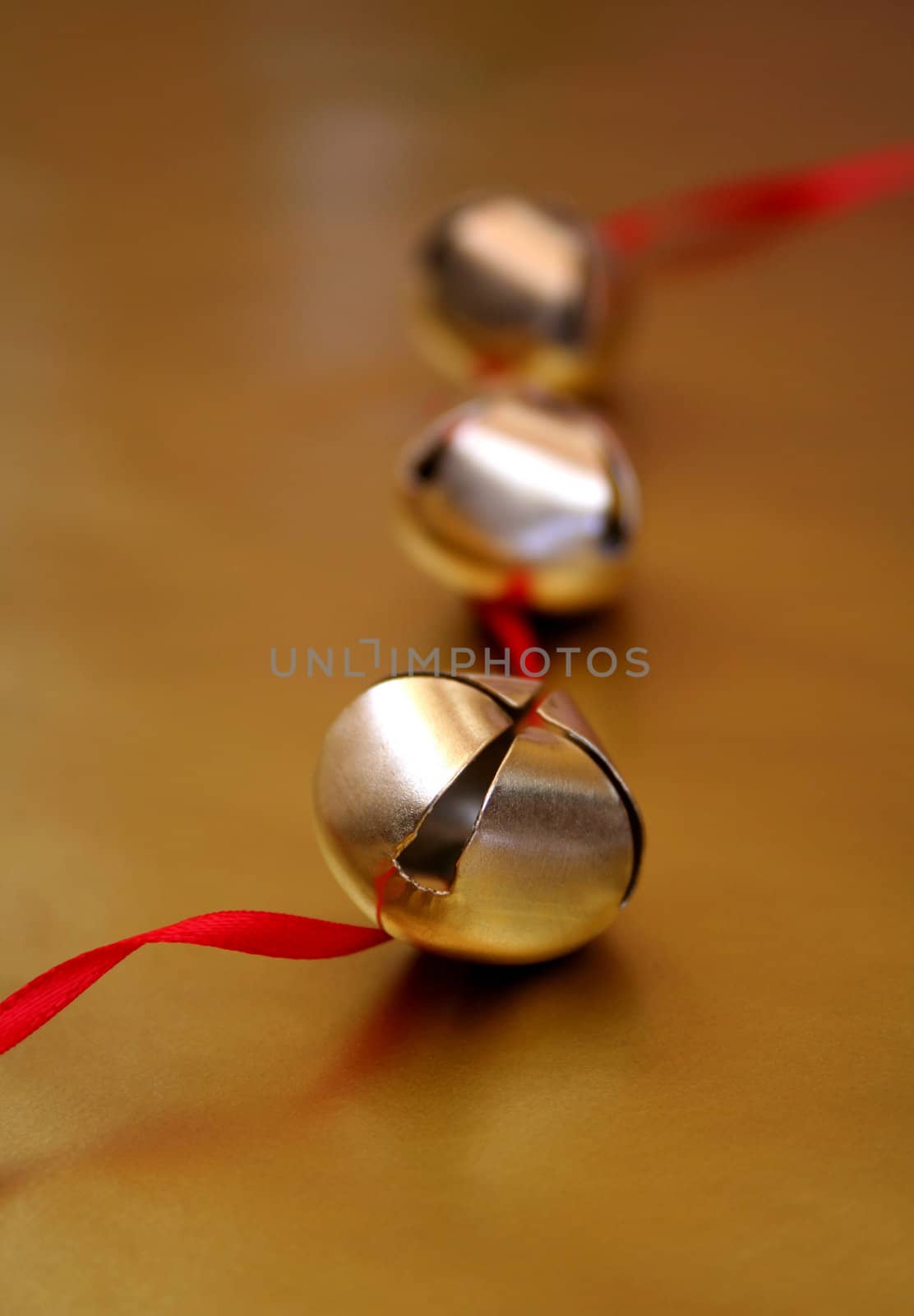 Three gold bells with red ribbon, all on a metallic gold background.