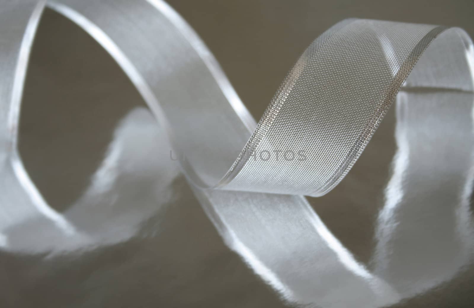 A piece of silver ribbon curled up on a metallic silver background. Shallow depth of field and selective focus.