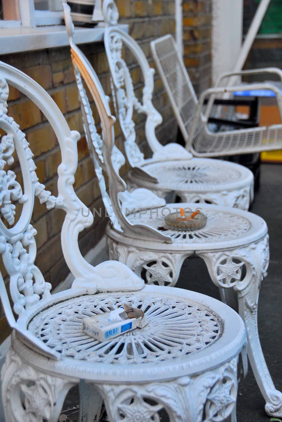 Empty chairs in the garden look like they have been waiting with someone for someone else. Now only cigarets remind about anyones presence.