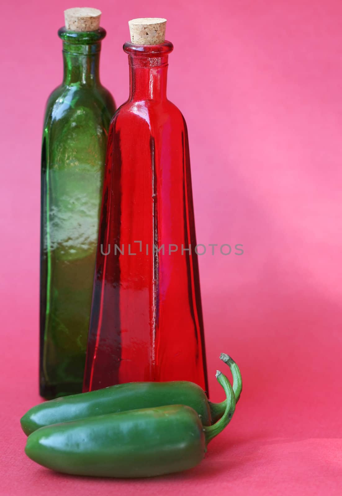 Glass bottle with a cork in the top and jalapeno peppers in front Shot against a red background