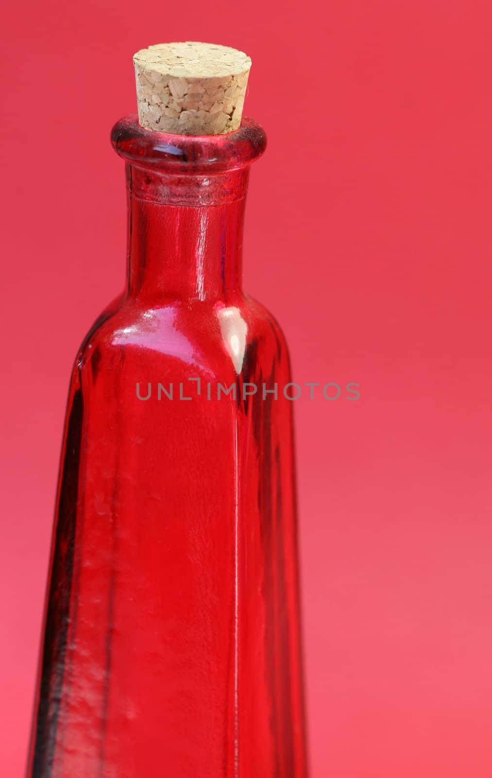 An emtpy red glass bottle with a cork in the top. Shoot against a red background