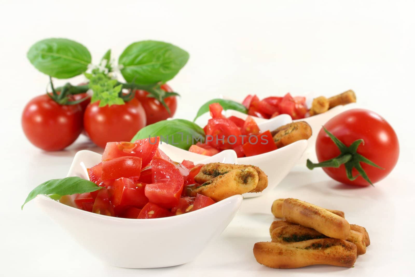 some bread sticks, tomatoes and basil on a light background
