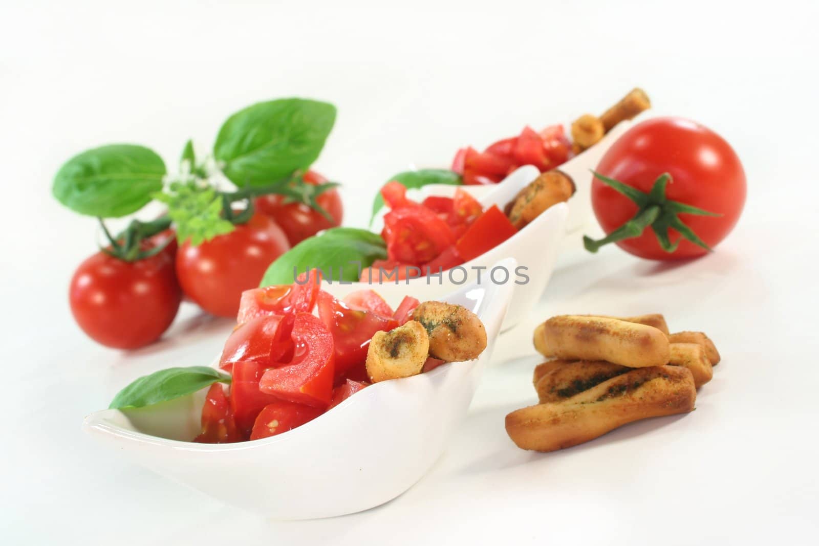 some bread sticks, tomatoes and basil on a light background
