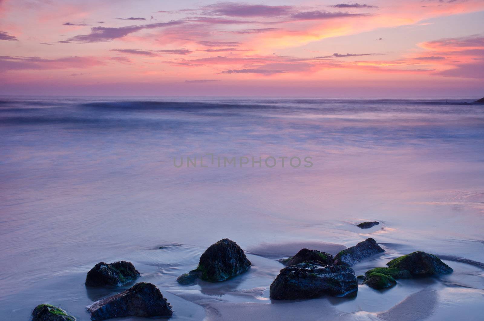 Sunset on a beach, beautiful sky and silky water arround rocks.