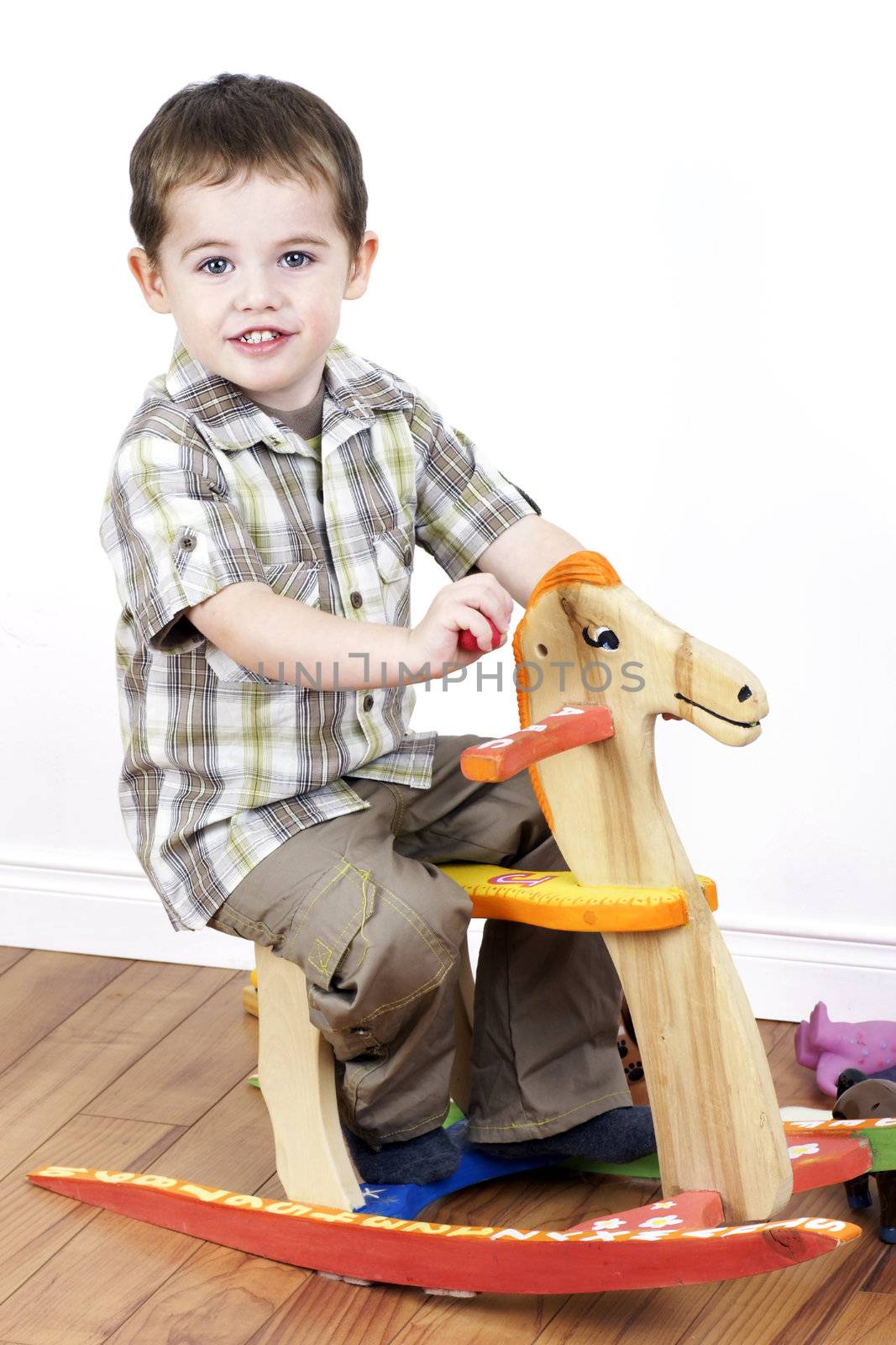 Cute little boy riding a handcarfted wooden rocking horse chair, vertical studio shot.