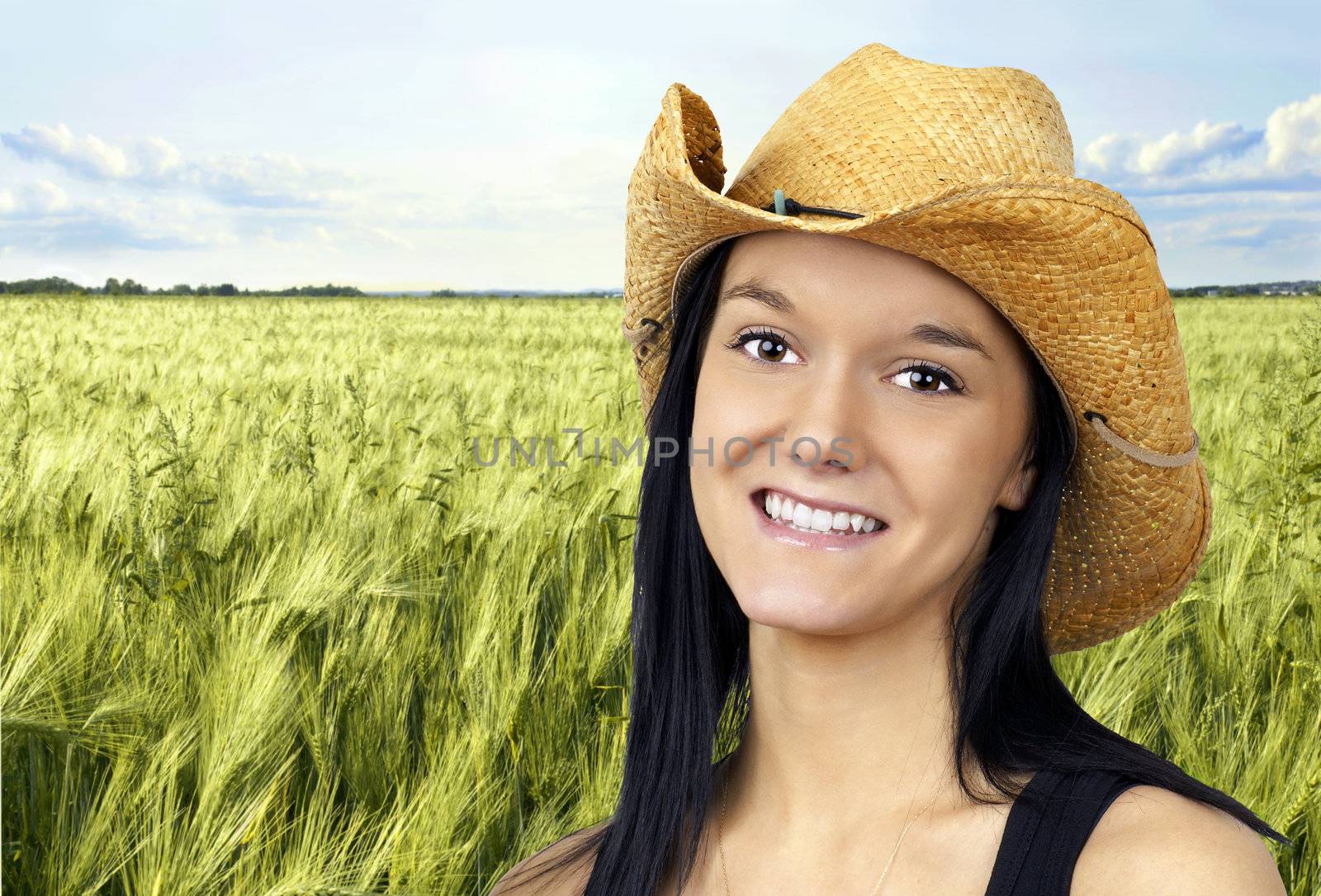 Pretty young cowgirl wearing a straw cowboy hat smiling and making the peace sign with her fingers.