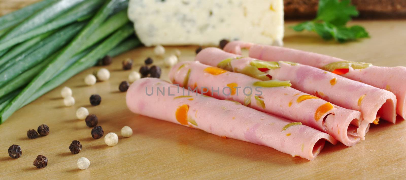 Cold cut slices on wooden board with pepper corns and shallot and cheese in the background (Selective Focus, Focus on the front of the first two slices)