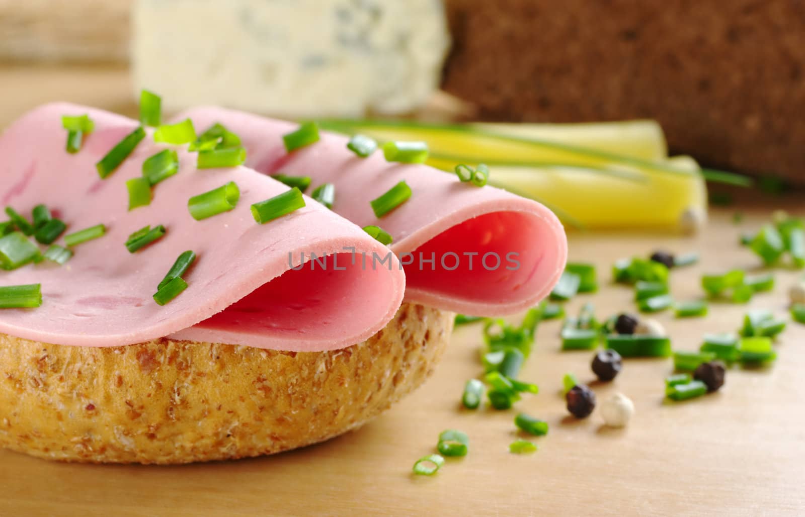 Two slices of cold cut on wholewheat bread garnished with chives. Peppercorns, bread and cheese in the background (Very Shallow Depth of Field, Focus on front of the first cold cut slice)