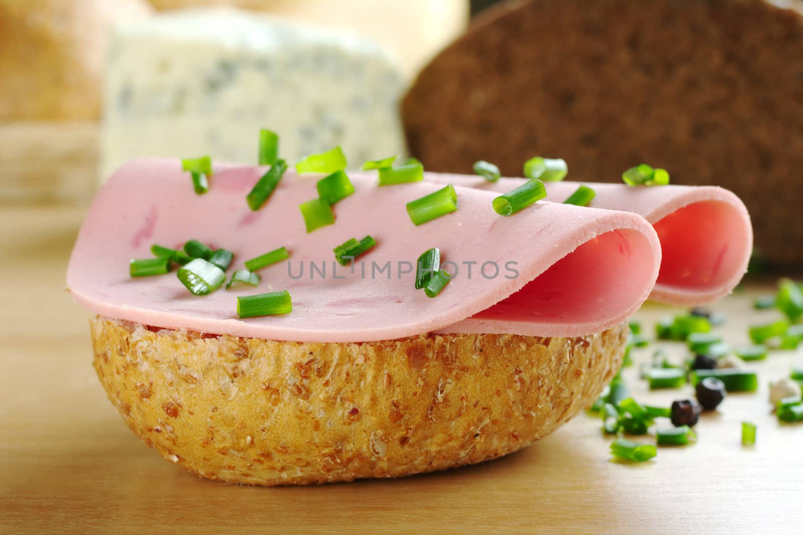 Open wholewheat sandwich with two slices of cold cut and chives. Peppercorns, bread and cheese in the background (Selective Focus, Focus on the front of the sandwich)