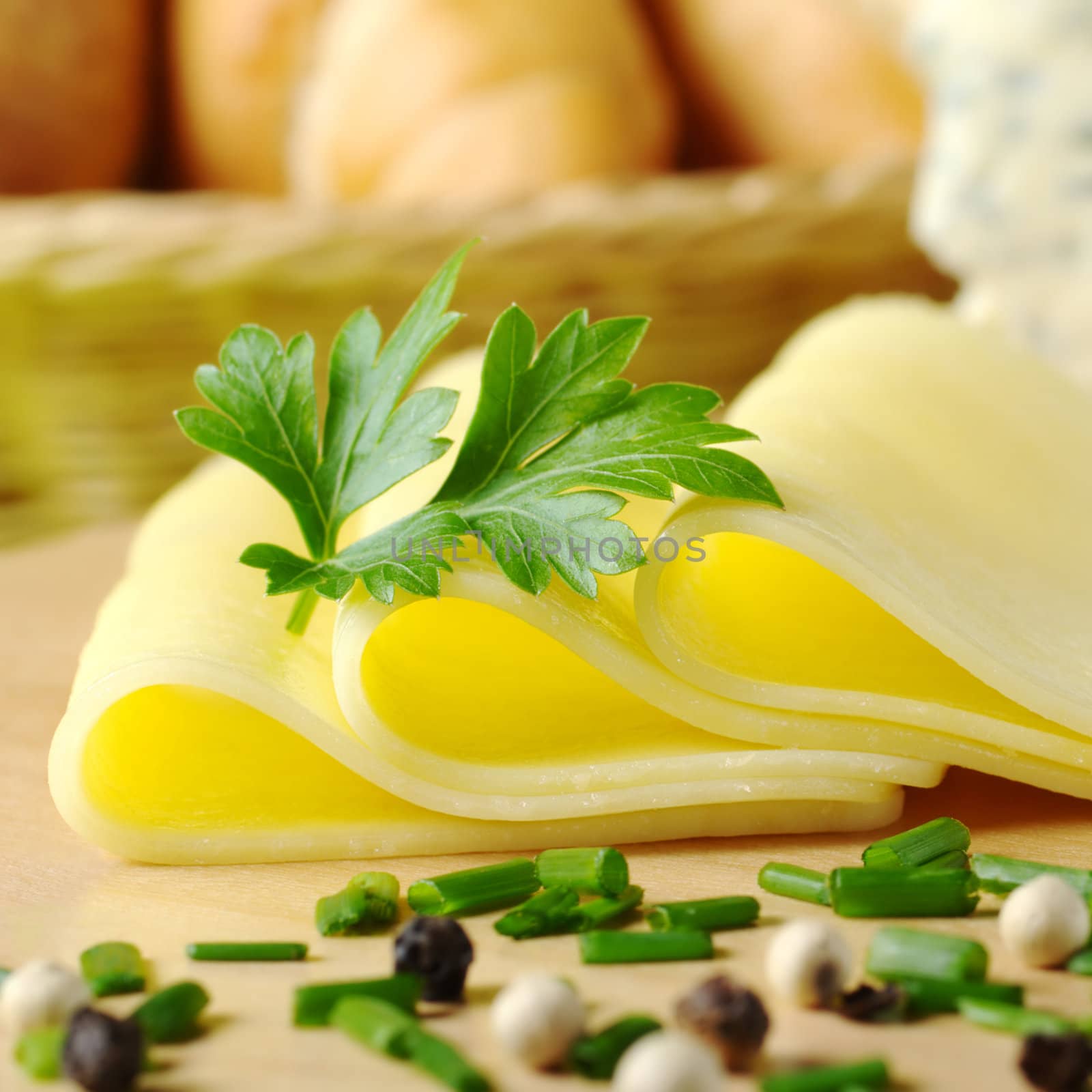 Cheese slices and parsley with chives and pepper corns in the front and bread basket in the back (Selective Focus, Focus on the front of the cheese slices and the parsley) 