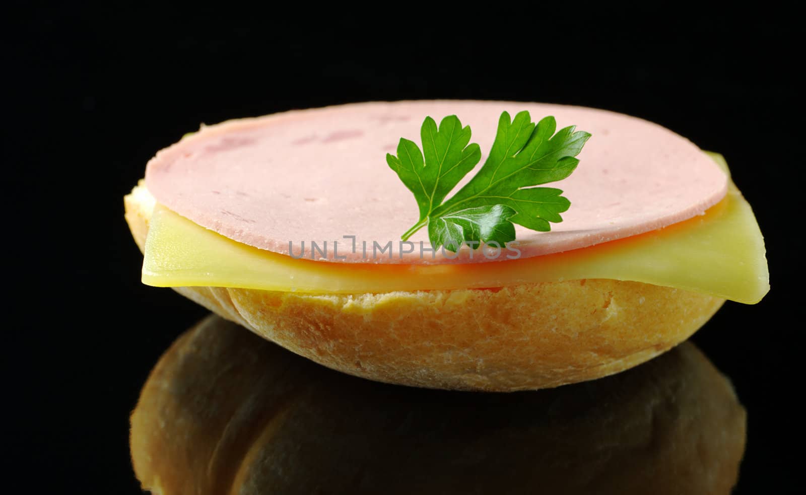 Open sandwich with a cheese and cold cut slice garnished with a parsley leaf photographed on black (Selective Focus, Focus on the front of the sandwich) 