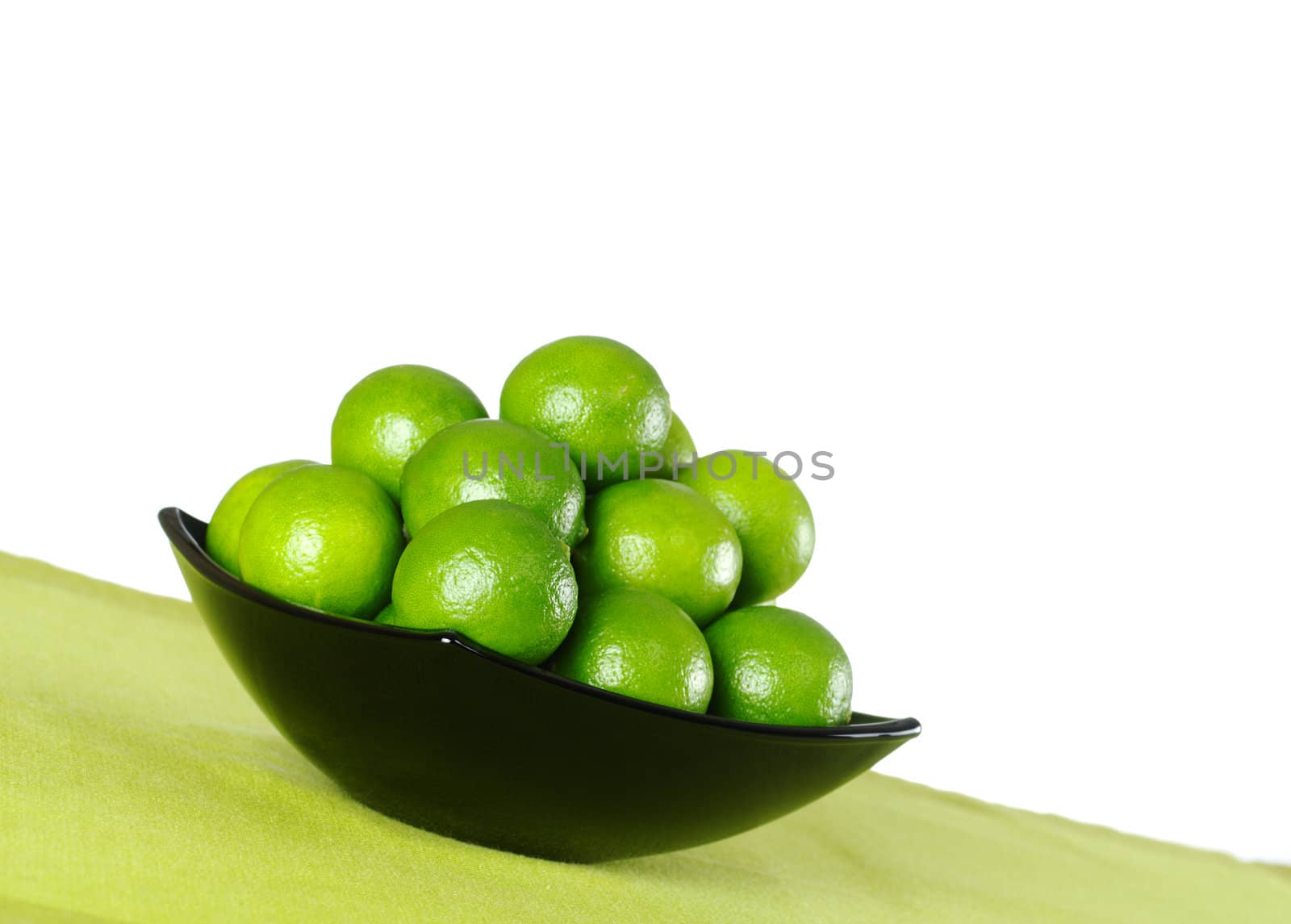 Green limes in black bowl on a green table mat with white background (Selective Focus, Focus on the lime in the front)