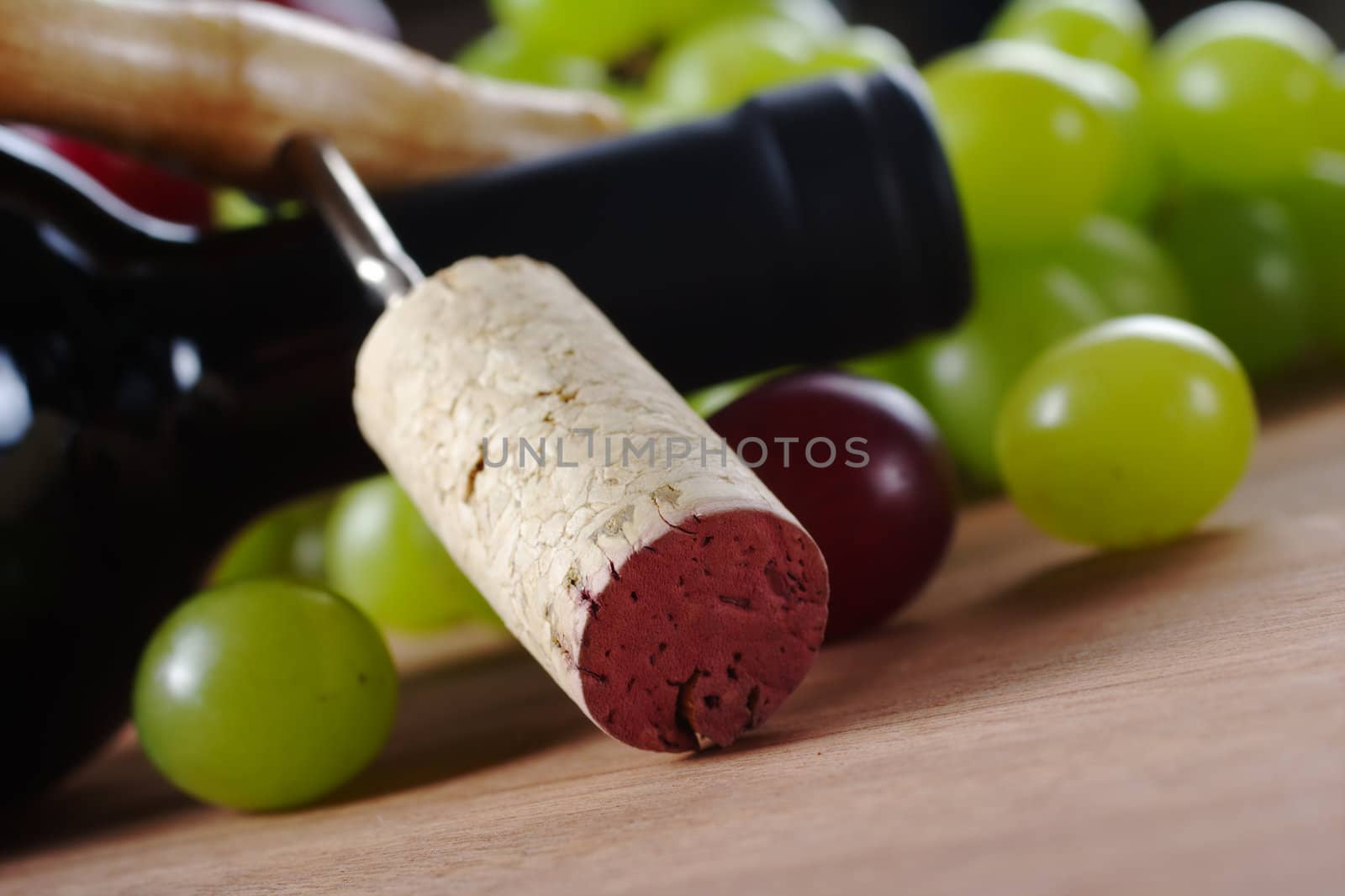 Cork on corkscrew leaning against a wine bottle surrounded by grapes (Very Shallow Depth of Field, Focus on the upper edge of the cork)