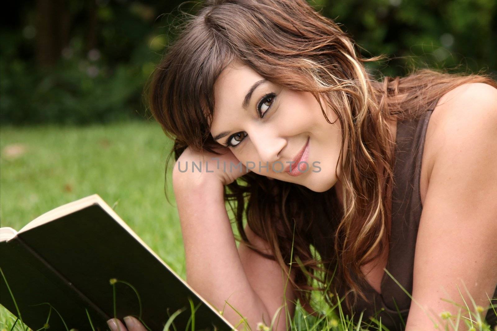 Pretty young woman laying on green grass and reading a book