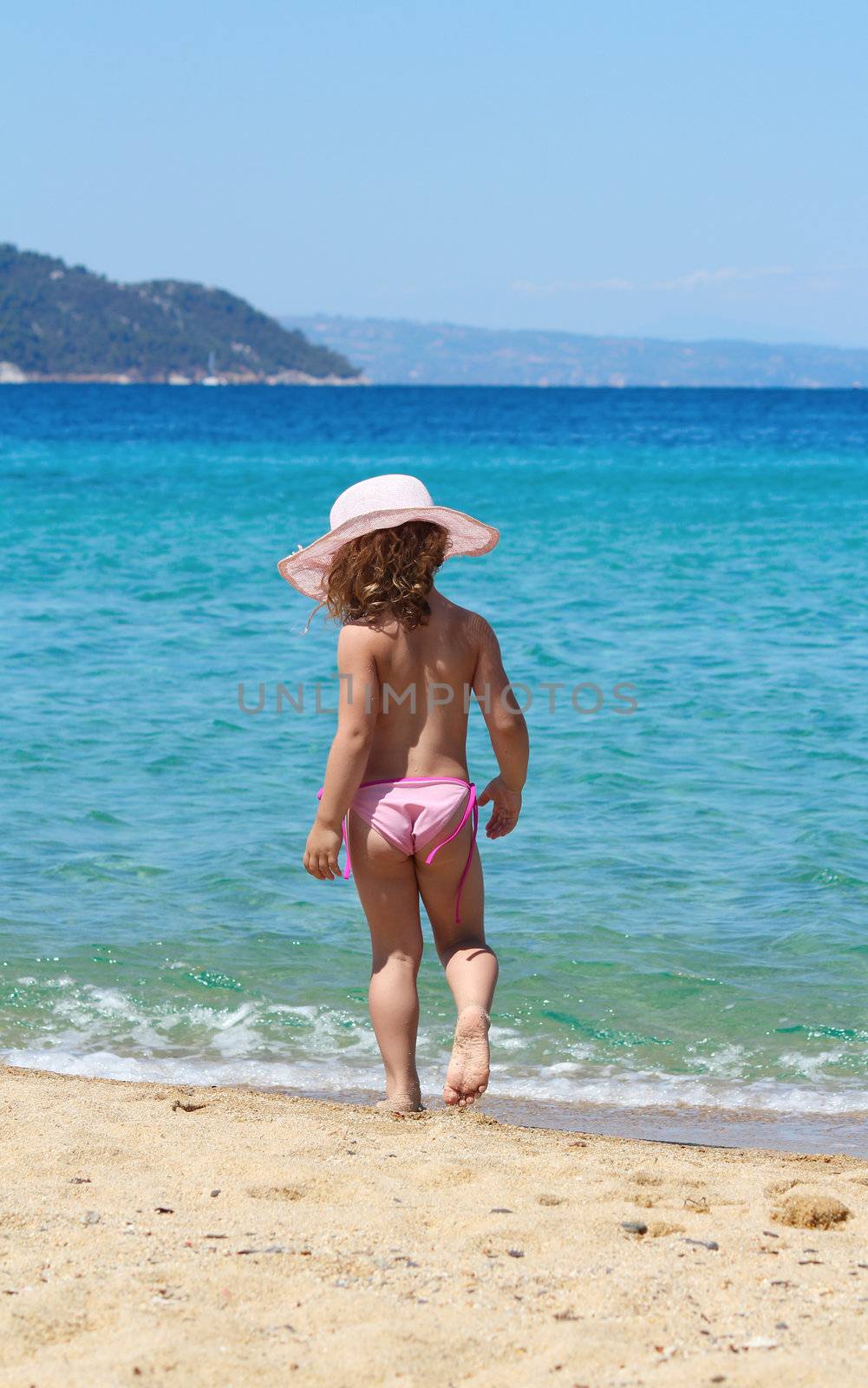 little girl with straw hat walking on beach