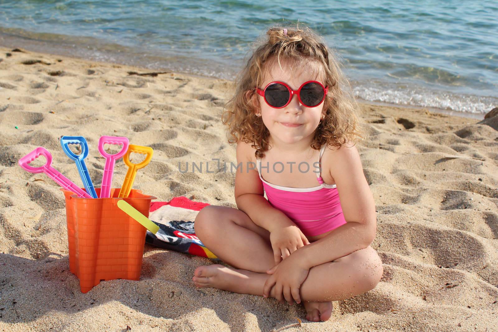 little girl with sunglasses sitting on beach by goce