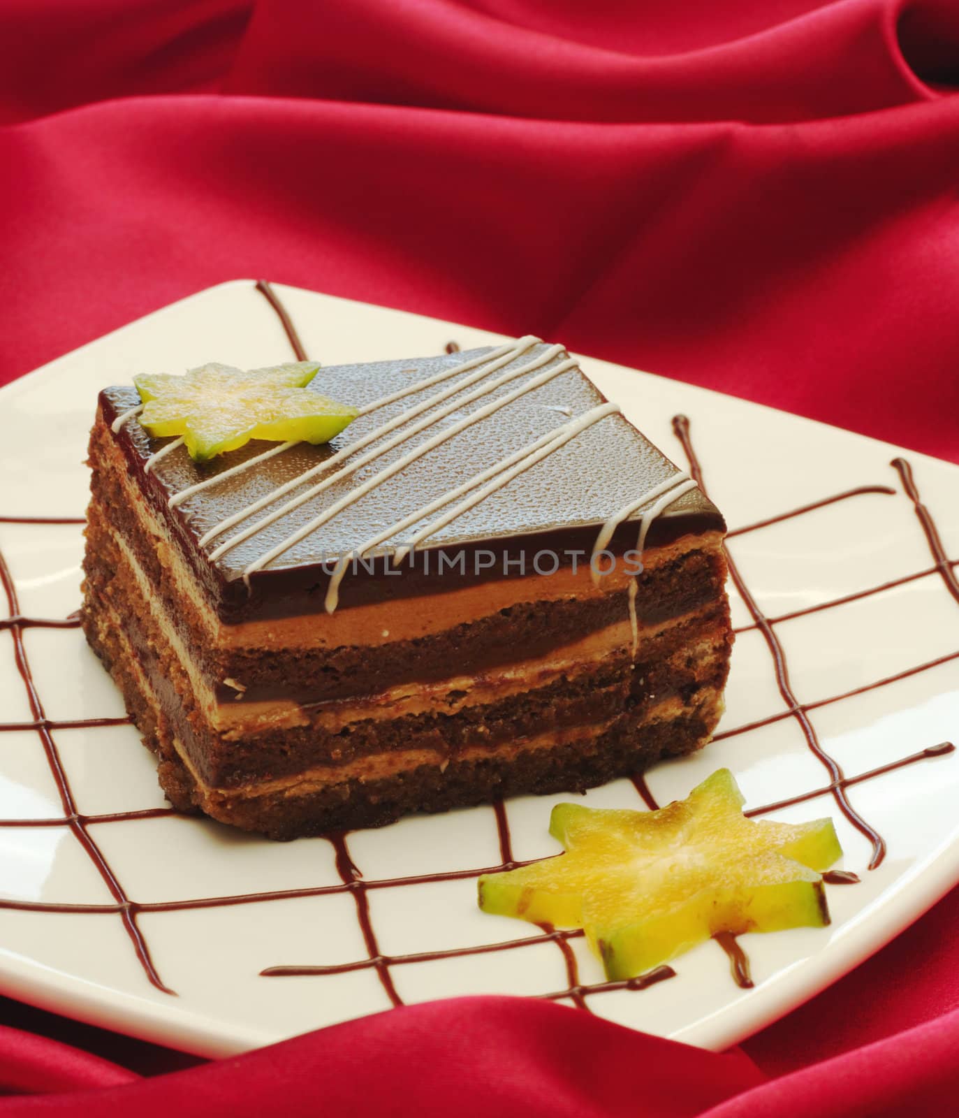 Tiramisu Cake on white plate with chocolate syrup and carambola as decoration on red fabric (Selective Focus)
