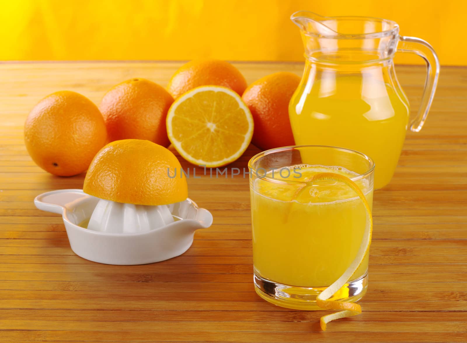 Fresh orange juice with orange juice squeezer, oranges and a jar of orange juice on wooden mat with orange background (Selective Focus)
