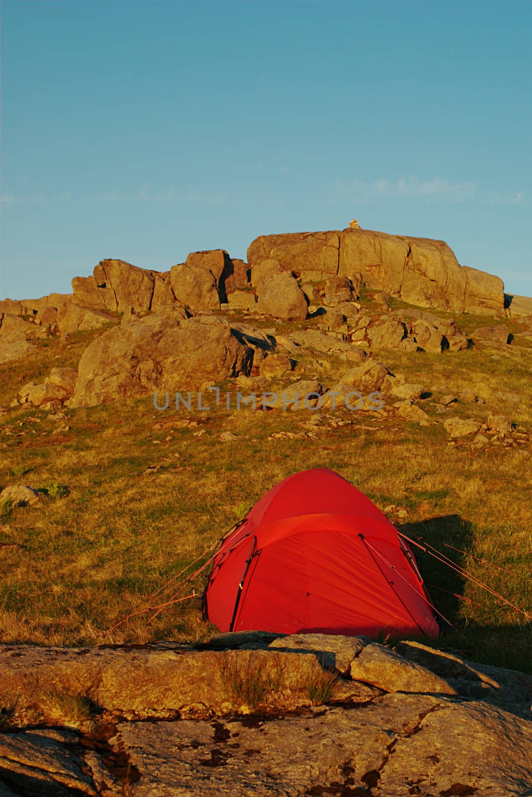 Red tent standing on mountain slope in yellowish evening sky