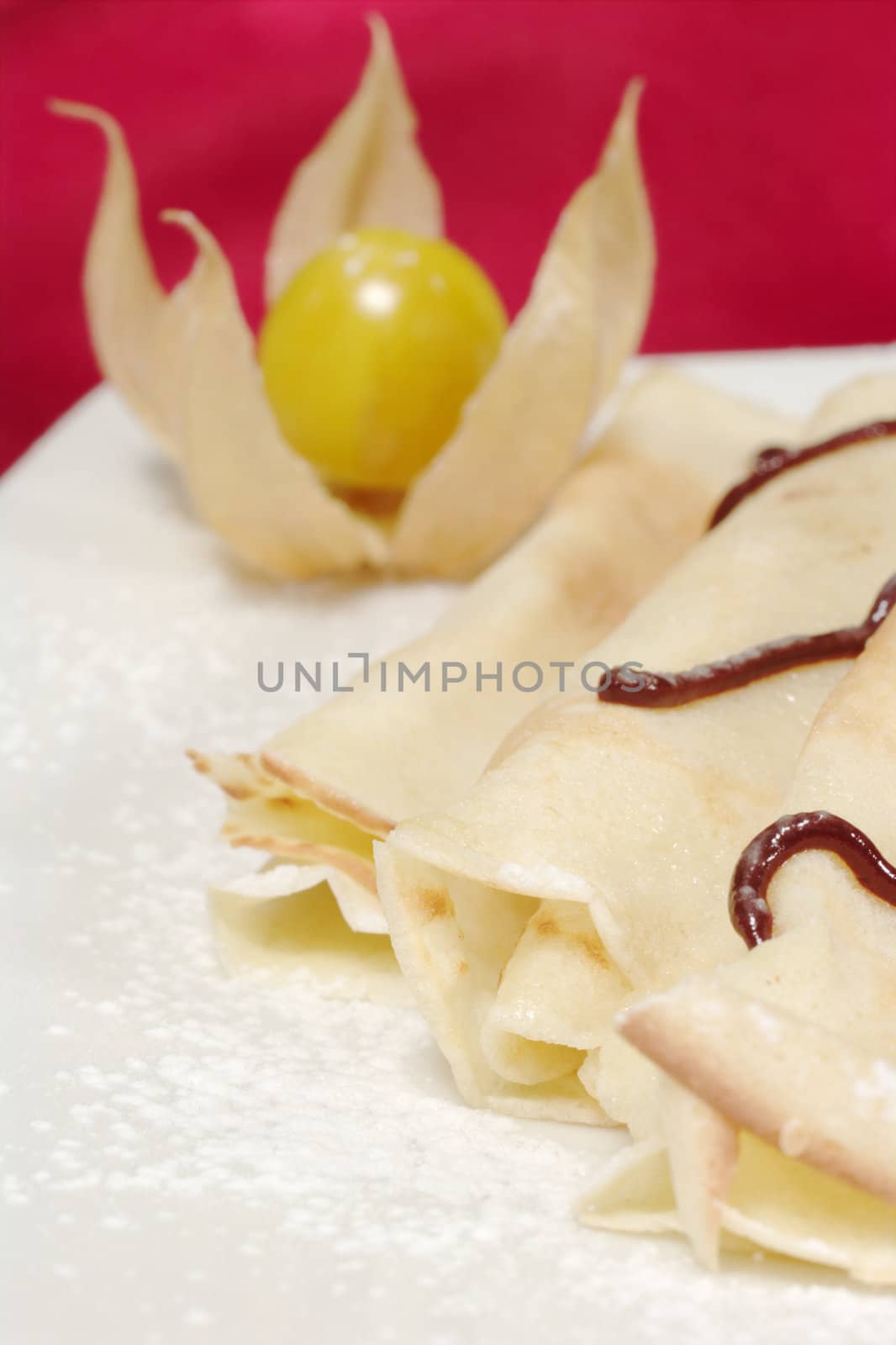 Palatschinken (Pancakes) with chocolate and powdered sugar on a plate and a physalis fruit as decoration