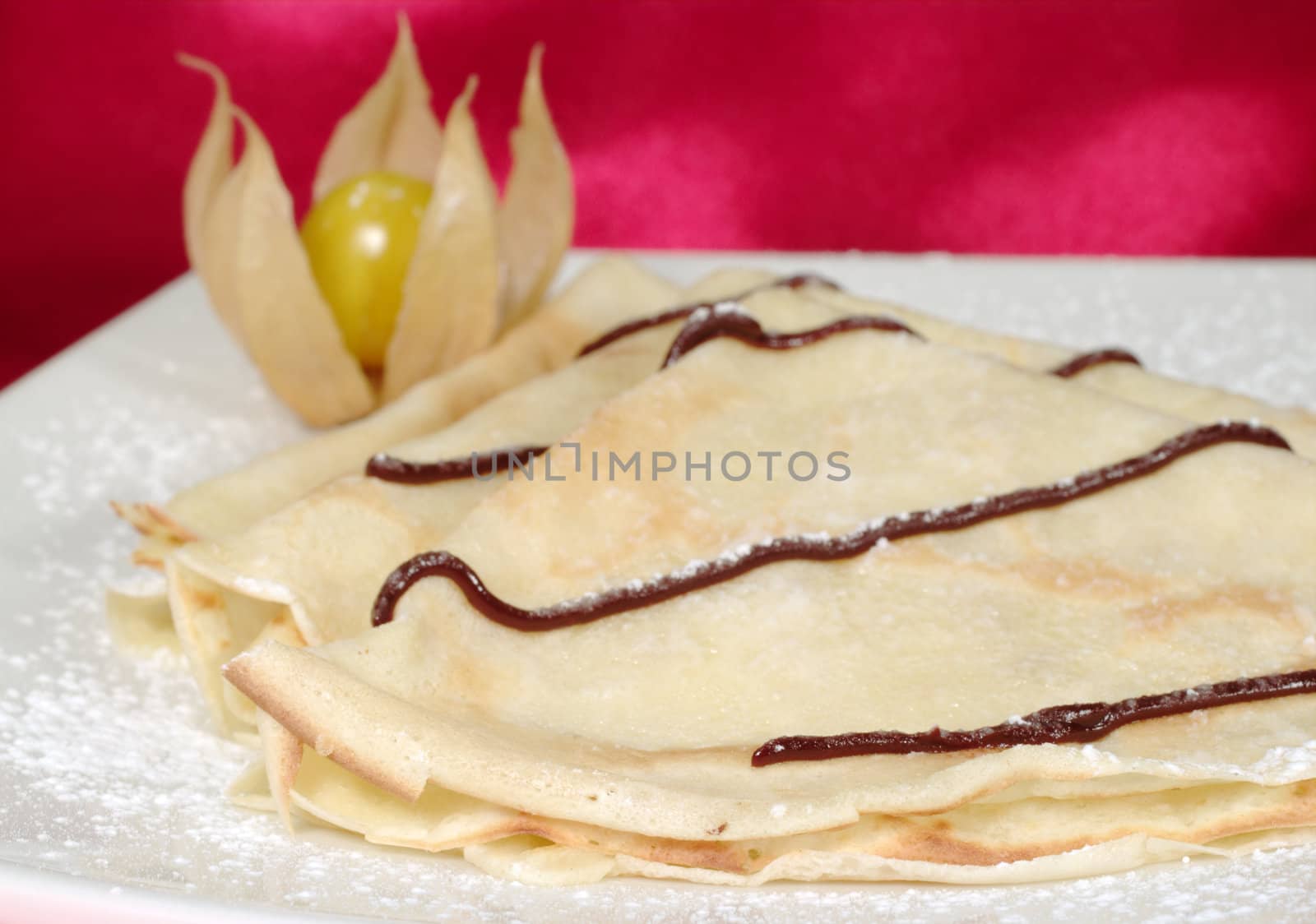 Palatschinken (Pancakes, Crepes) with chocolate and powdered sugar on a plate and a physalis fruit as decoration