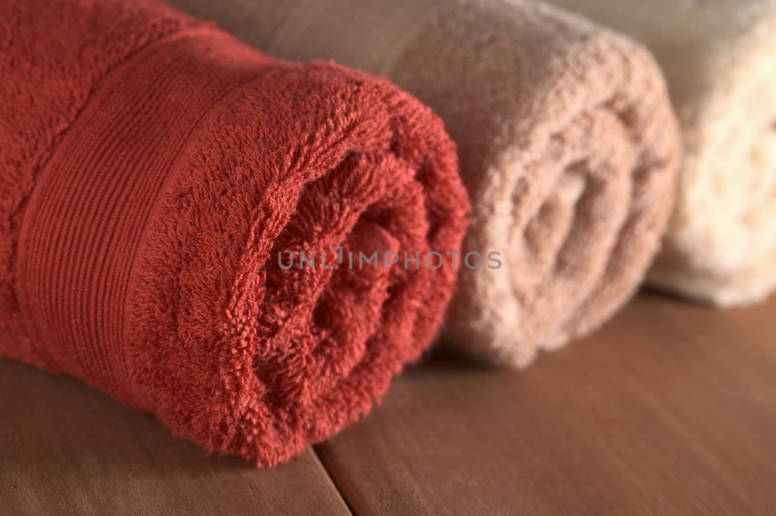 Different colored rolled up towels on wood (Selective Focus, Focus on the front edge of the red towel)