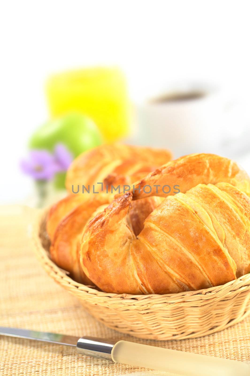 Fresh croissants in bread basket with coffee, orange juice and a green apple in the back (Selective Focus, Focus on the front of the croissant)