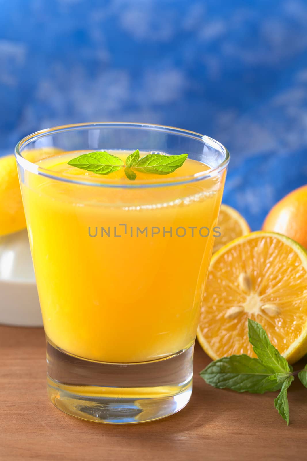 Freshly squeezed orange juice with orange slice and mint leaf on top of the juice with a blue background (Selective Focus, Focus on the mint leaf on top of the juice)