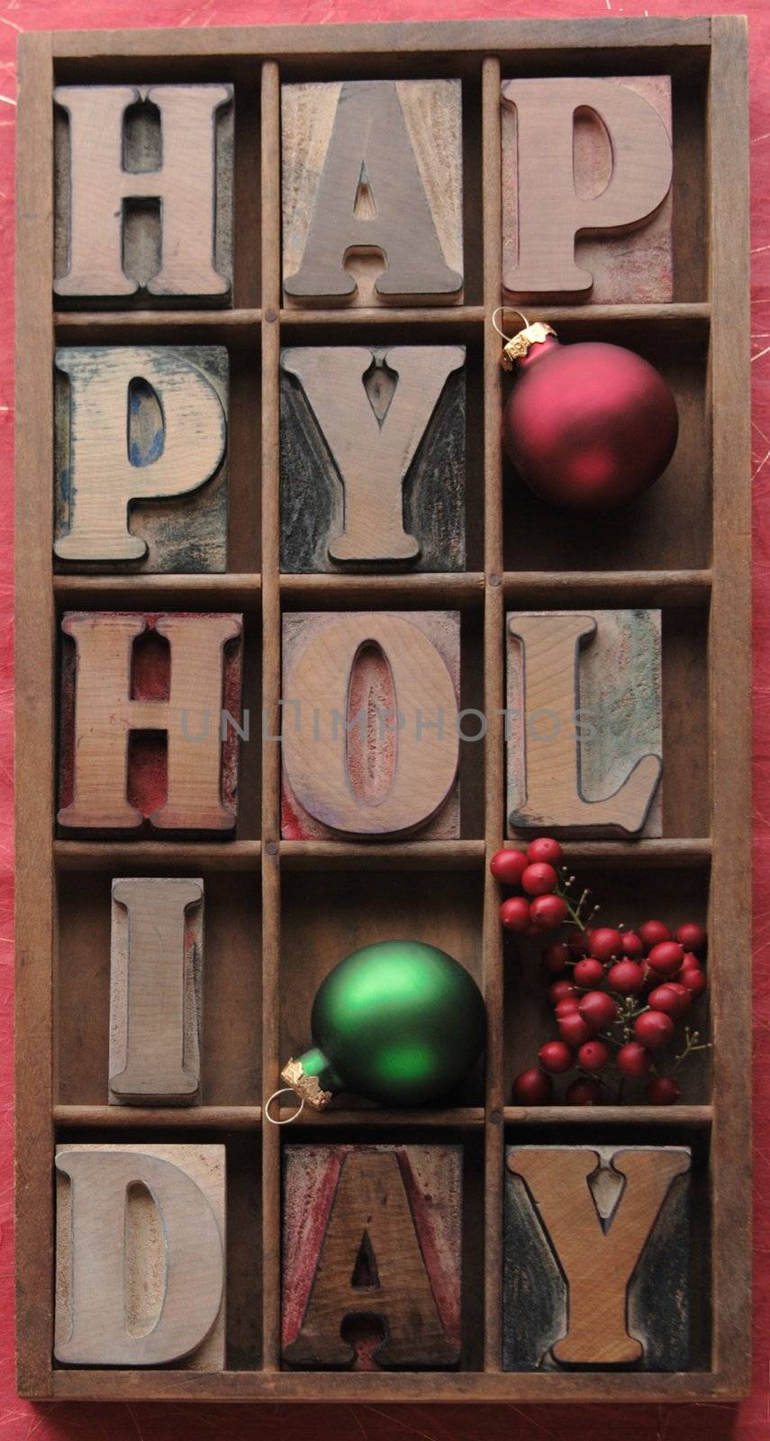 happy holiday in old wood letters in a type case with ornaments and berries