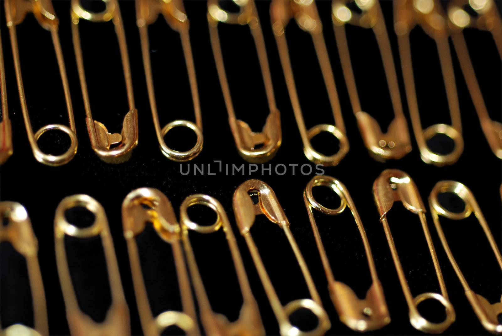 Rows of shiny golden safety pins on a black background