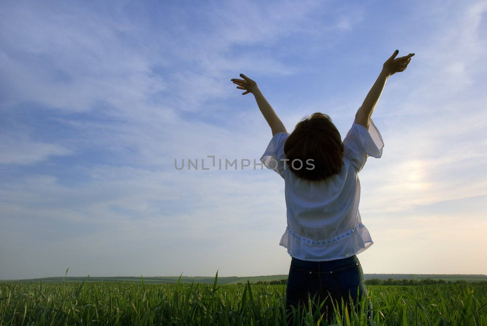 Concept - freedom. The girl photographed behind on a background of a sunset above a wheaten field