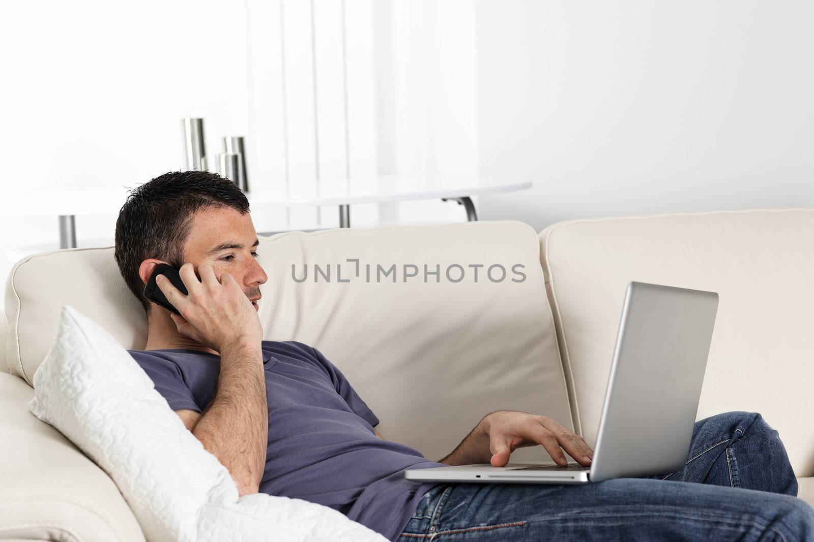 beautiful young man on sofa with computer and phone