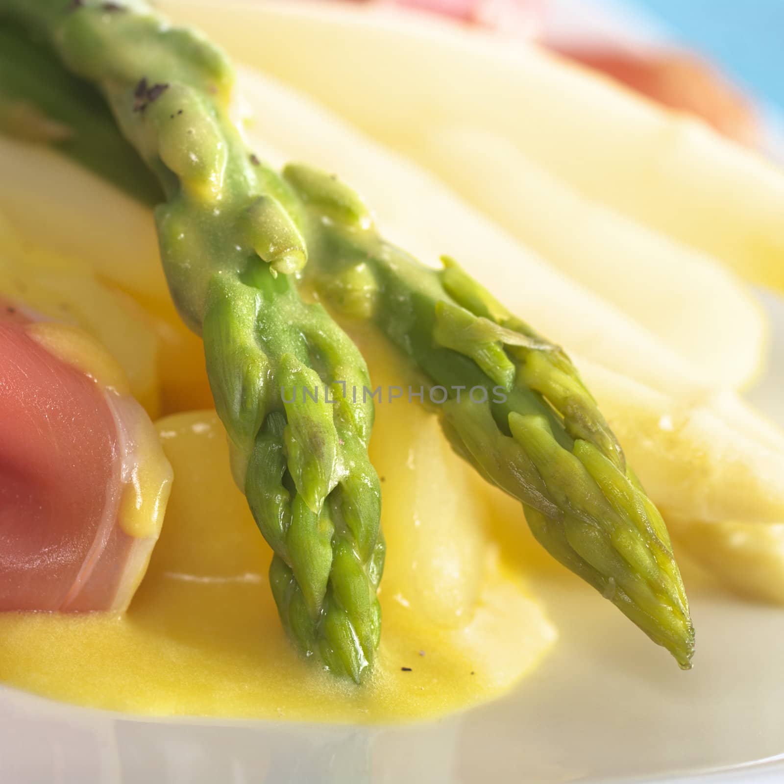 Green asparagus on cooked potato pieces with Hollandaise sauce on top and ham slices on the side (Selective Focus, Focus on the asparagus heads)