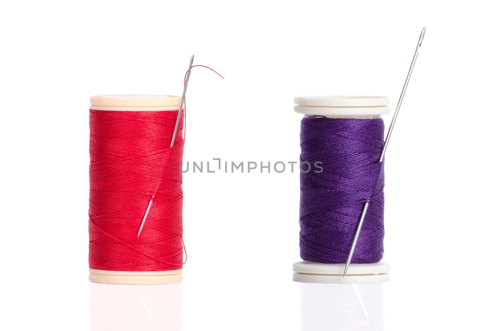 Two red and purple thread bobbin and needle isolated on white background.
