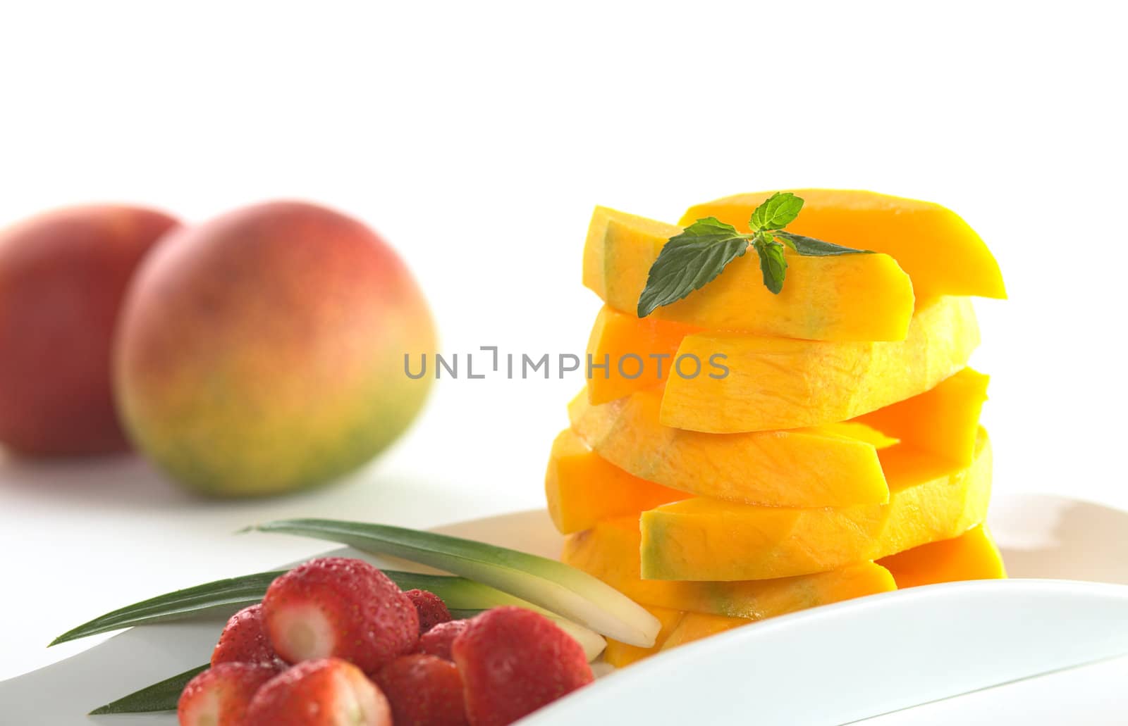 Mango sticks arranged in a pile garnished with mint leaf and strawberries in the foreground (Selective Focus, Focus on the mint leaf and the front of the mango pile)
