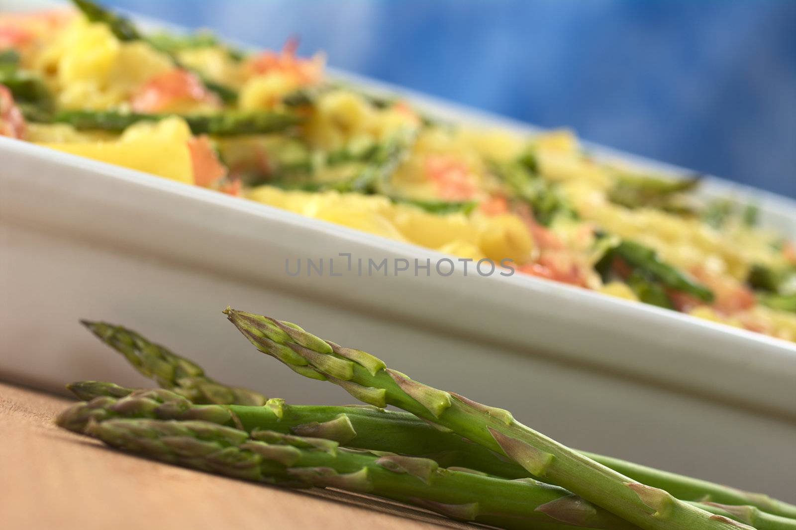 Fresh raw green asparagus with asparagus-ham-macaroni casserole in the back (Selective Focus, Focus on the head of the asparagus on top)