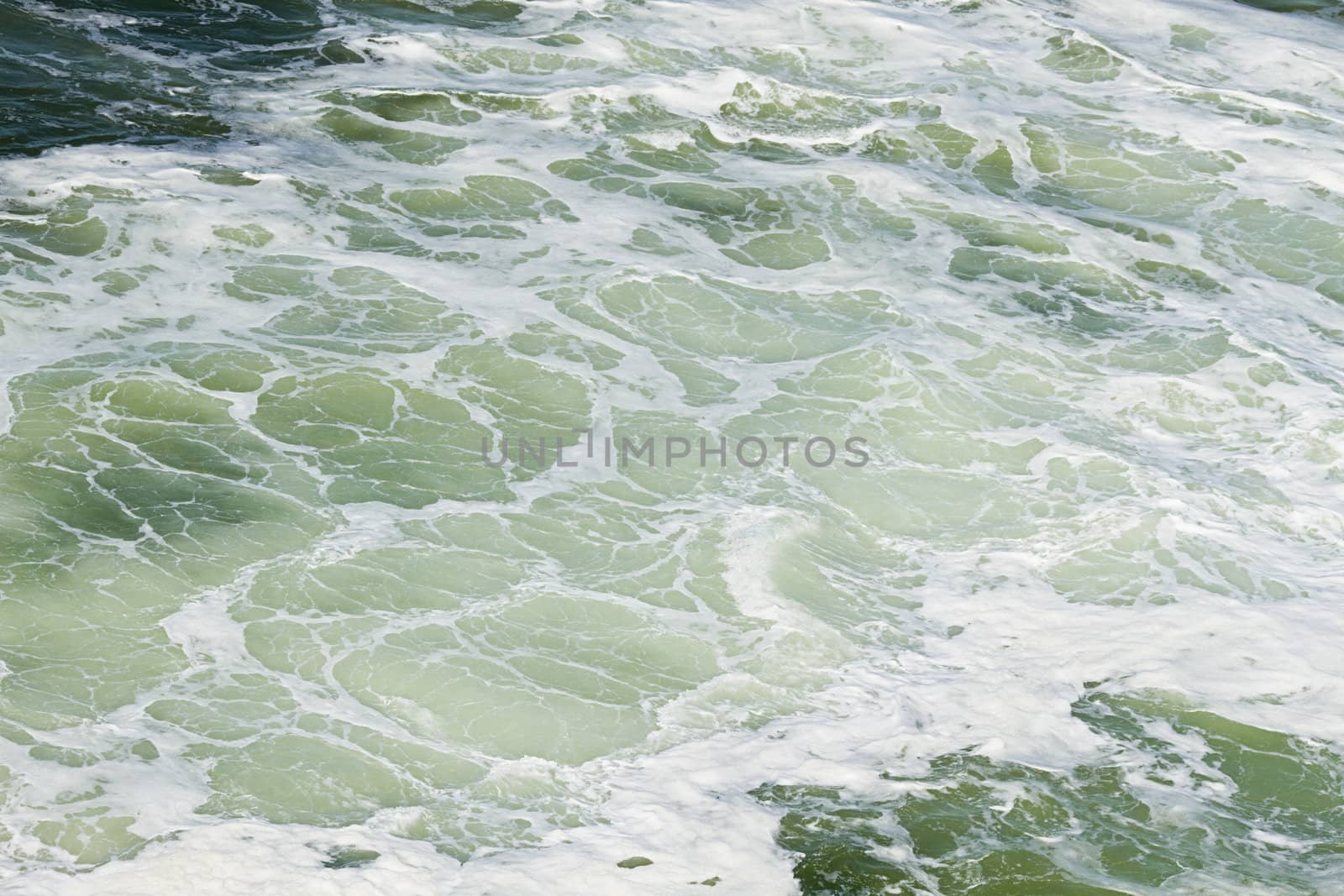 Foam on the water made by turning ship giving a light green color to the water