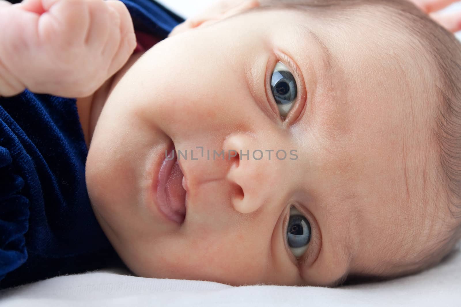 A cute newborn baby girl happily smiling and sticking out her tongue.
