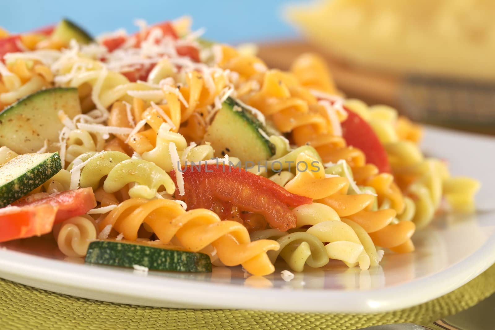 Colorful fusilli pasta with zucchini, tomato and grated cheese (Selective Focus, Focus on the tomato in front)
