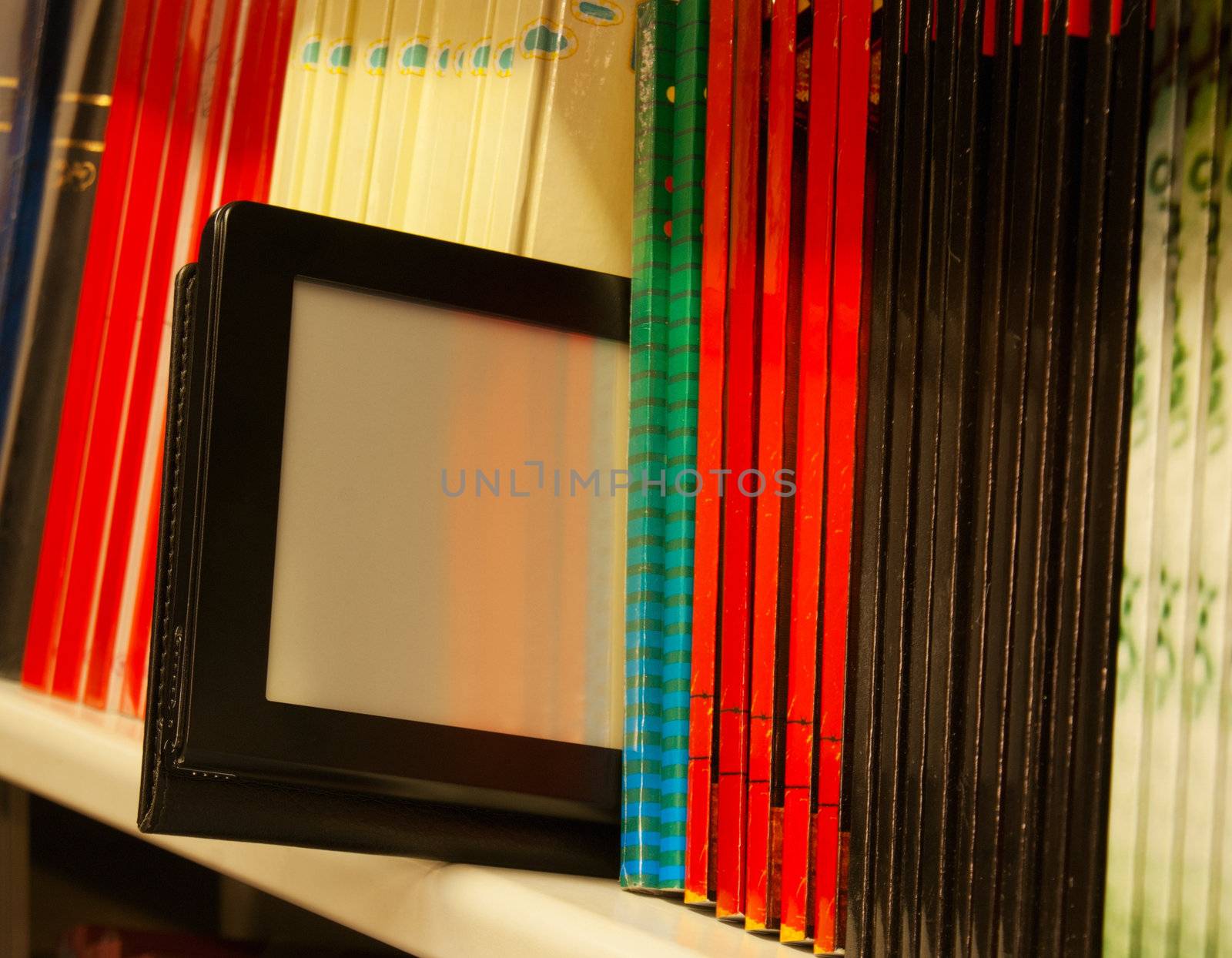 Row of colorful books and electronic book reader on the shelf