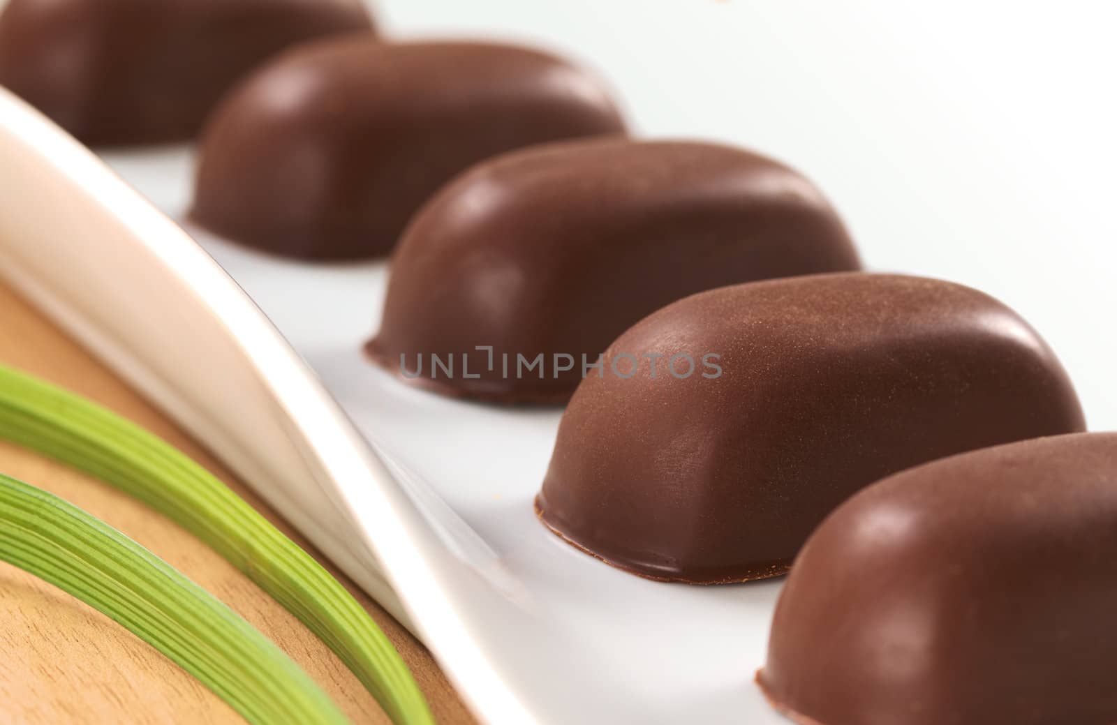 Chocolate candies filled with pecan nut arranged on a long white plate  (Very Shallow Depth of Field, Focus on the front of the second candy)