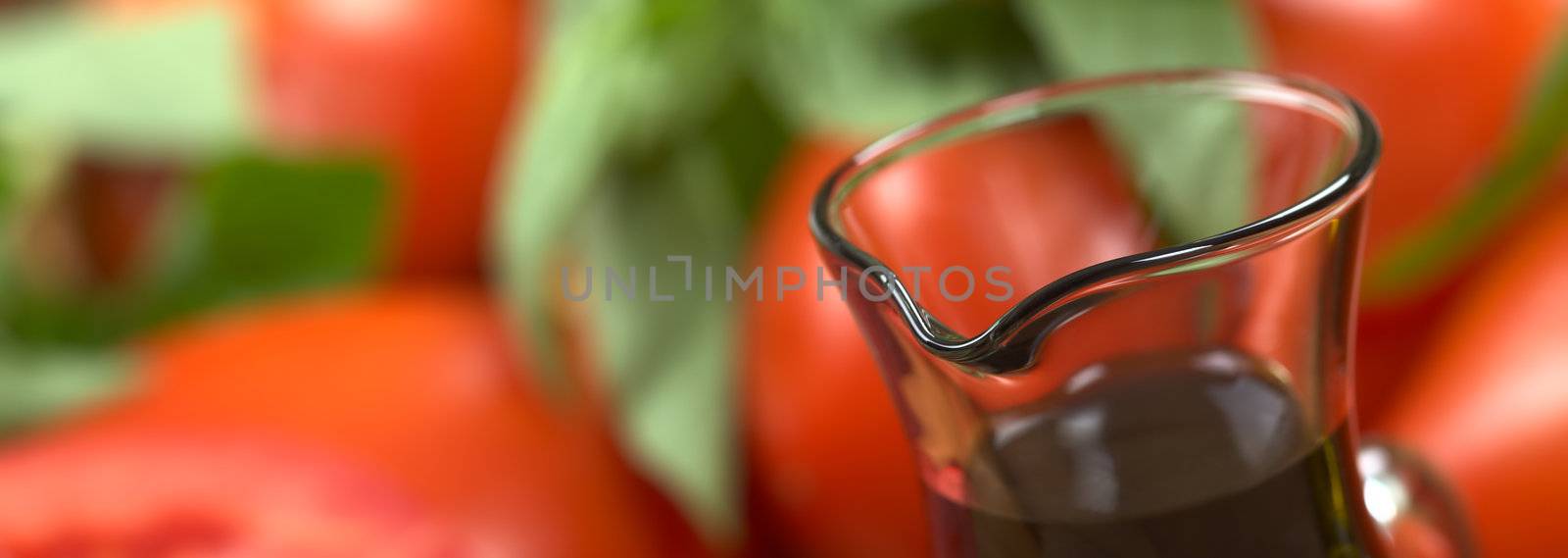 Balsamic vinegar with tomato and basil in the back (Very Shallow Depth of Field, Focus on the front of the bottle rim)