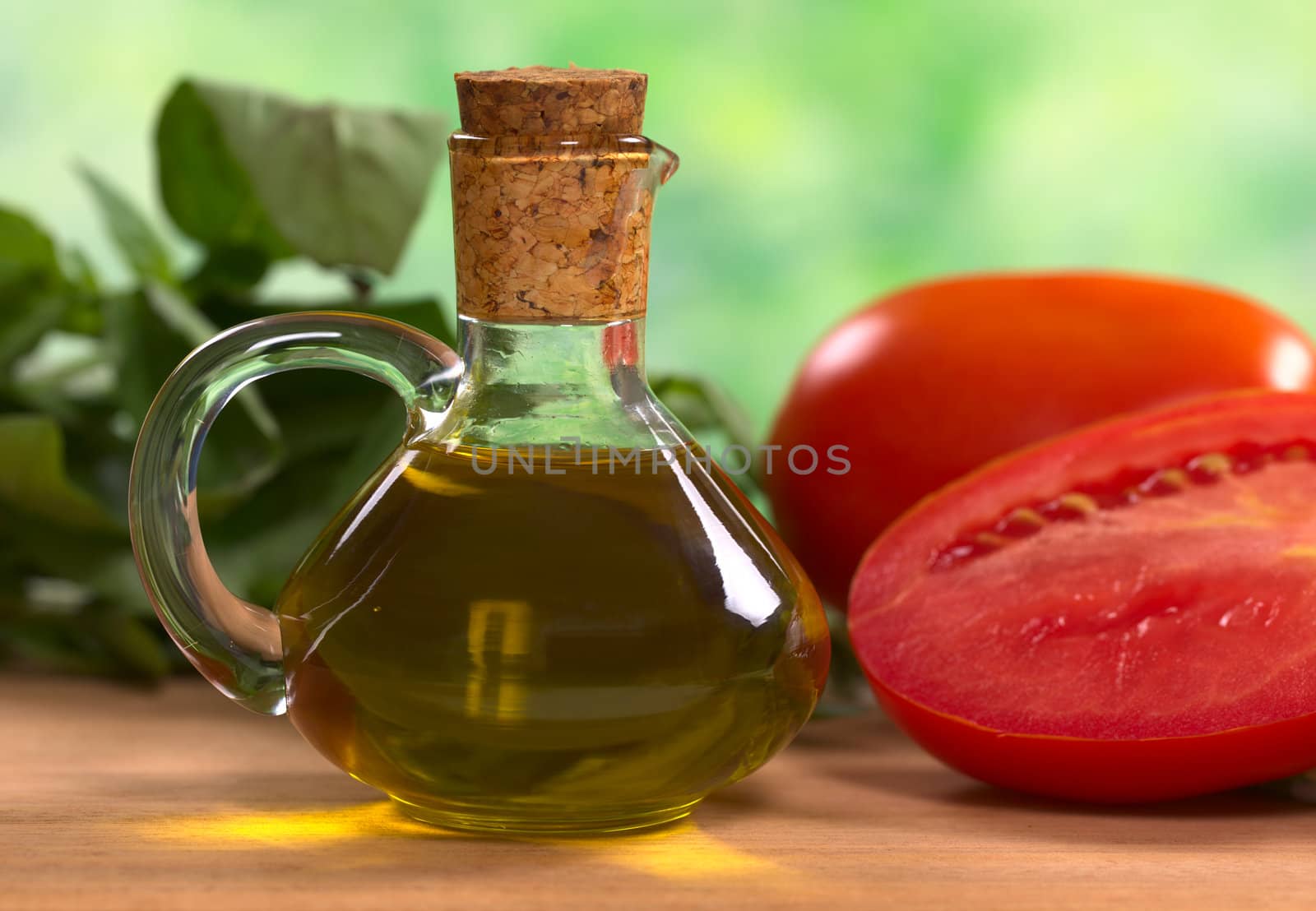 Olive oil with tomato and basil leaves in the back (Selective Focus, Focus on the front of the bottleneck and the handle)