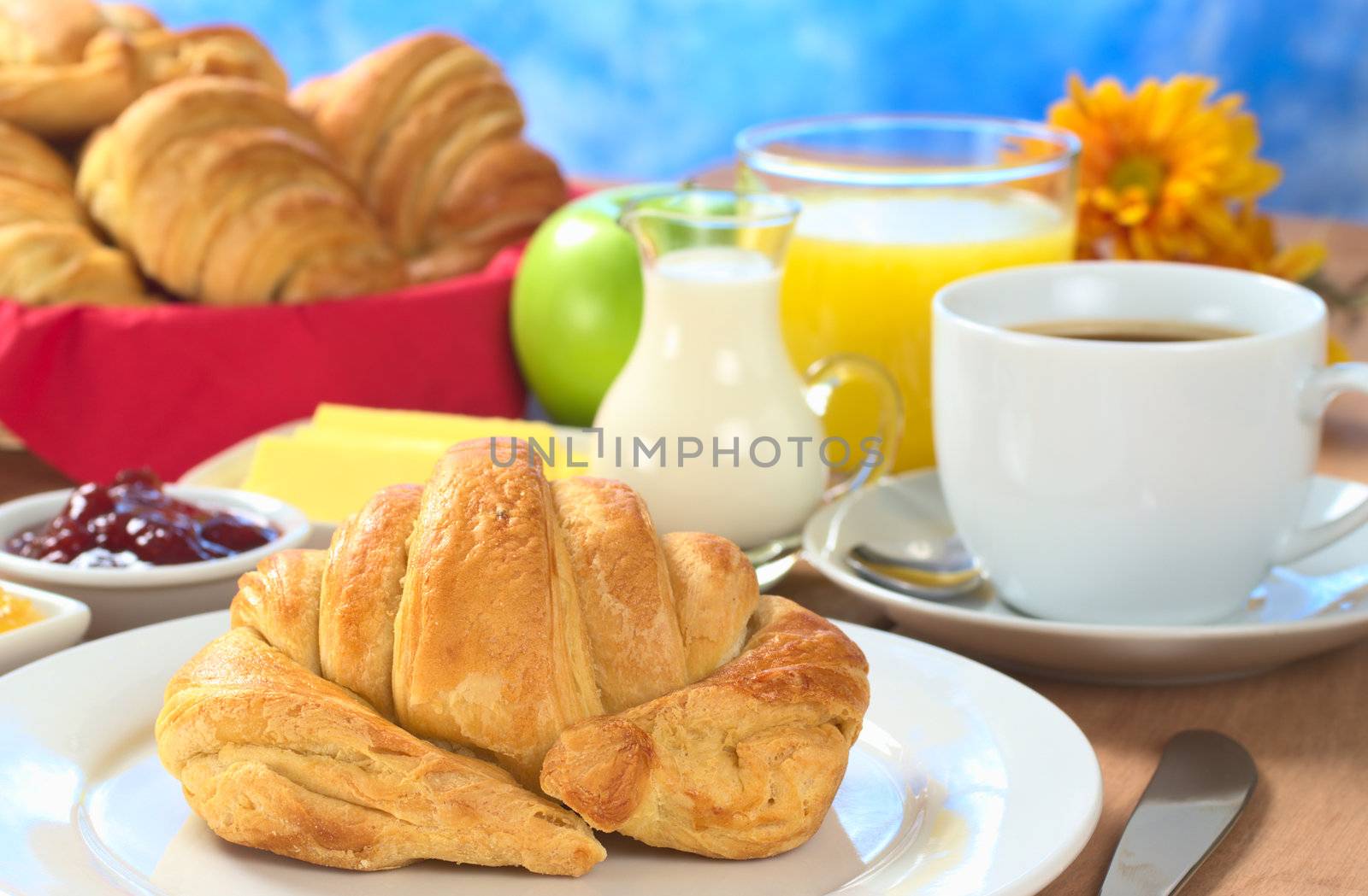 Continental breakfast with croissant, coffee, orange juice, milk, jam, butter and green apple (Selective Focus, Focus on the front of the croissant)