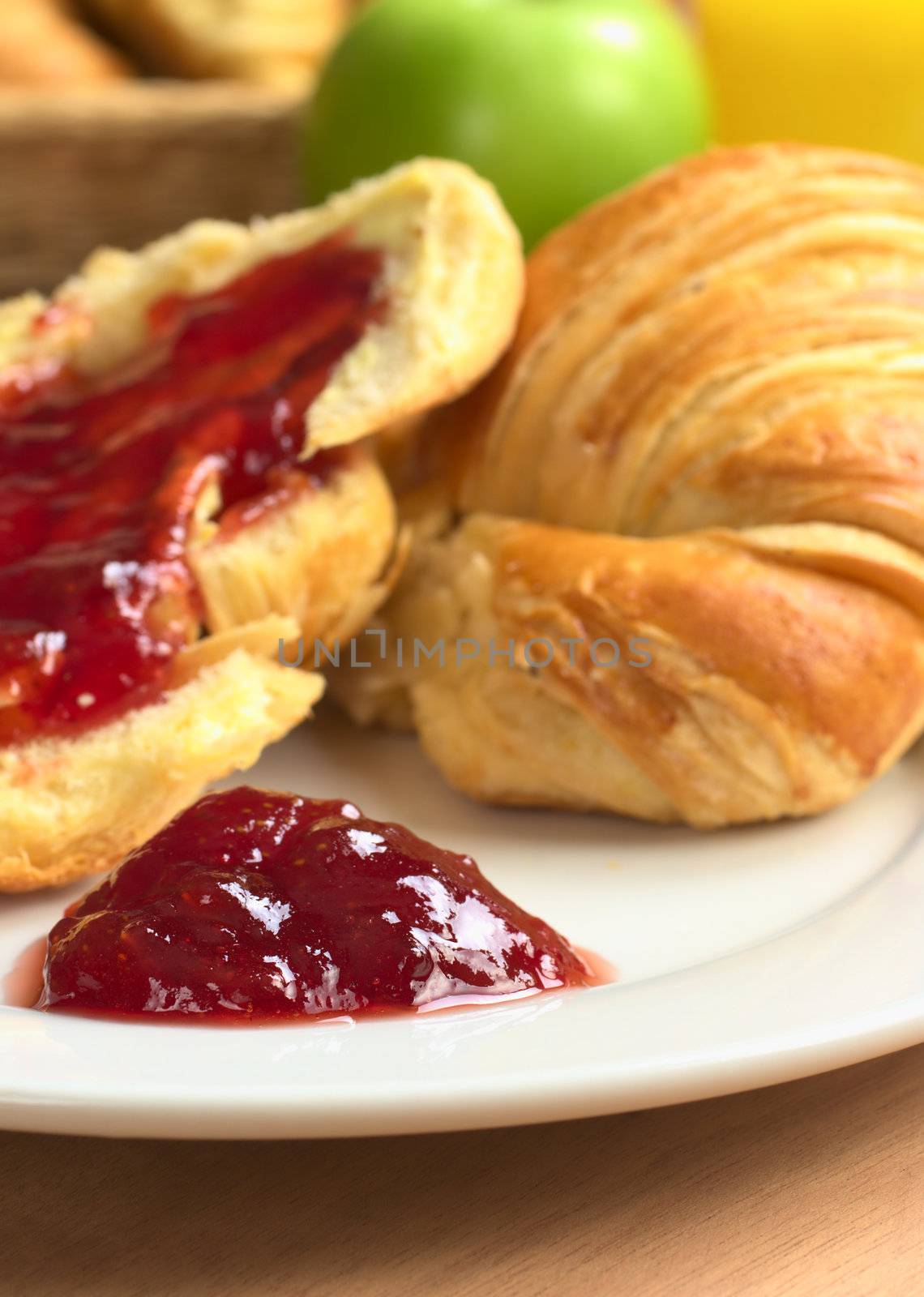 Strawberry jam on plate with croissant green apple and orange juice in the back (Selective Focus, Focus on the front of the jam pile)