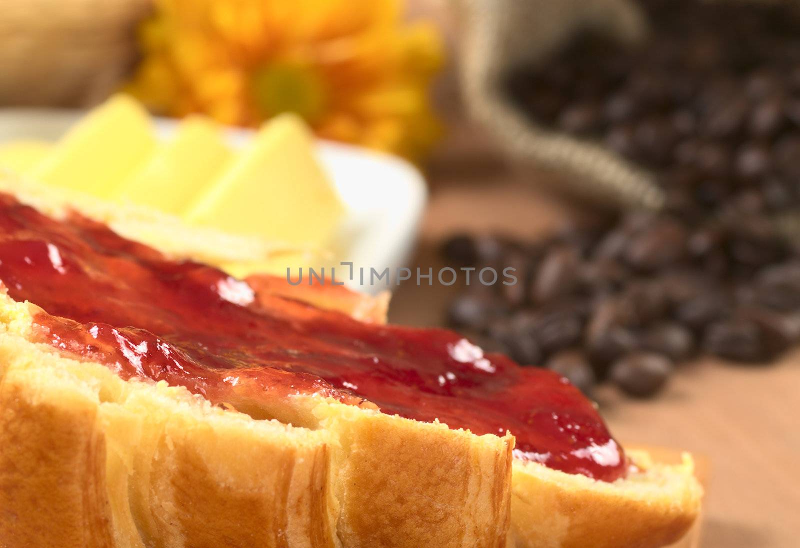 Strawberry jam spread on croissant with butter and coffee beans in the back (Selective Focus, Focus on the front of the spread jam)