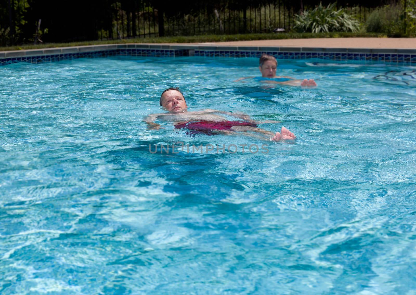 Baby boomer couple floating in a backyard swimming pool on a hot summers day