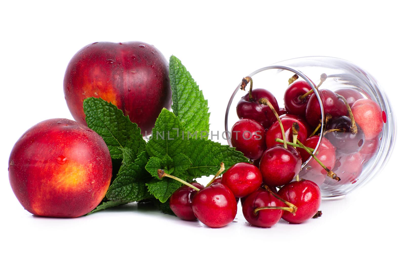 Set of red fruits, cherries on a glass, peaches and mint leaves isolated on white background.