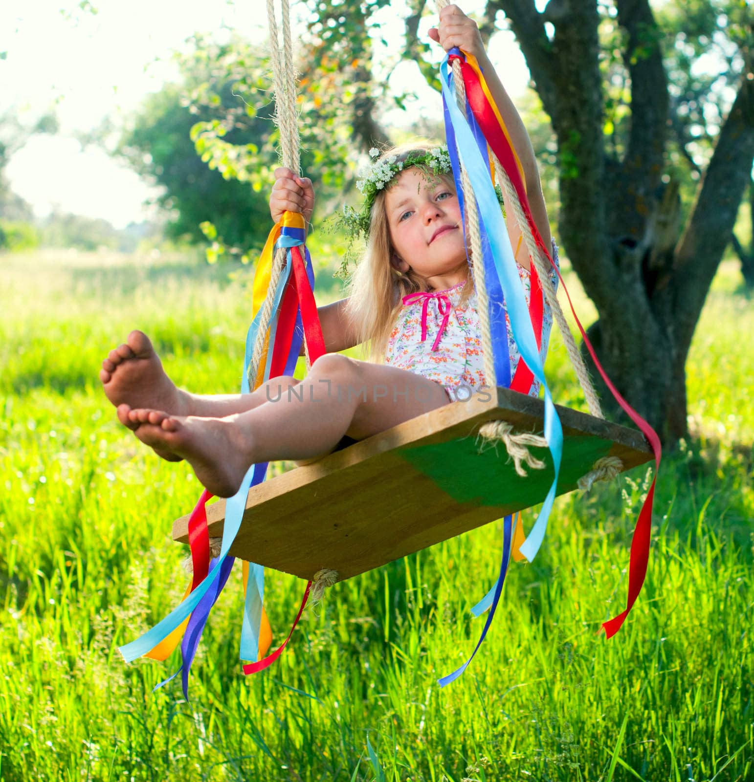 Young cute girl on swing with ribbons in the garden